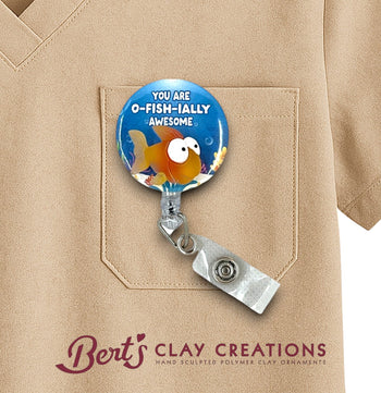 Badge holder with fish design and text 'You are o-fish-ally awesome' on a beige shirt, branded with 'Bert's Clay Creations'.